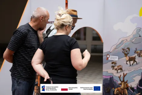 Grupa osób – kobieta w średnim wieku uczesana kok oraz dwóch mężczyzn w średnim wieku – jeden w kapeluszu słomkowym czytający napisy na jednej ze ścianek wystawowych. 