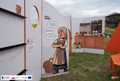 Plansza wystawy plenerowej z ilustracją kobiety z XVI wieku i sceną przedstawiającą dawny sklep w tle. Na dole zdjęcia znajduje się pasek z logotypami Funduszy Europejskich, Rzeczypospolitej Polskiej i Unii Europejskiej.