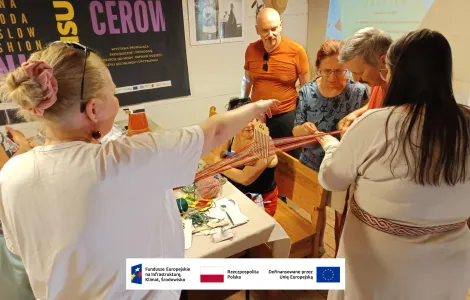 cztery kobiety oraz dwóch mężczyzn podczas warsztatów tkania krajki na tabliczkach. Dwie osoby trzymają rozwiniętą włóczkę, jedna osoba tłumaczy innym w jaki sposób wykonać splot