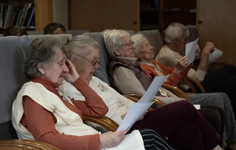 Na fotelach siedzi pięcioro starszych osób. Trzymają kartki, z których coś czytają.